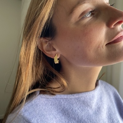 Brincos dourados de três barras em mulher com cabelo castanho e camisa cinza