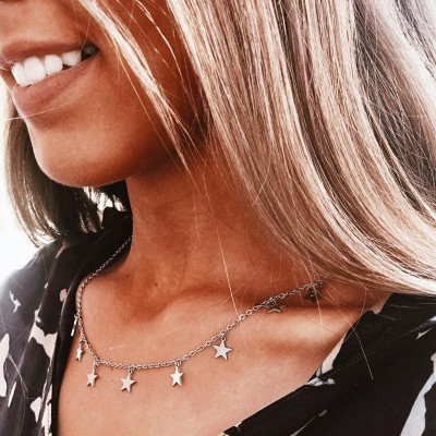 Colar de prata com pendentes de estrela no pescoço de uma mulher.