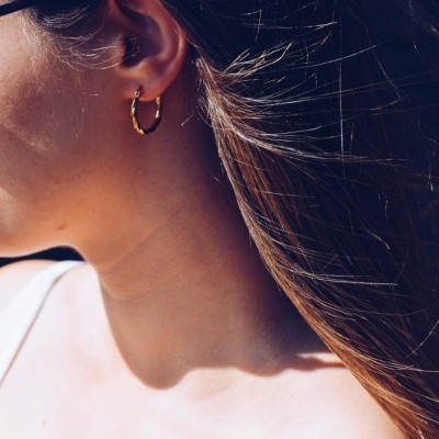 Brinco de argola dourado com textura torcida numa mulher com cabelo castanho