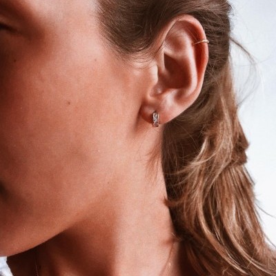 ouvido com brincos prateado e dourado, cabelo castanho claro, fundo branco