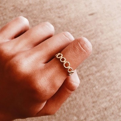 Anel dourado com padrão de círculos entrelaçados no dedo médio
