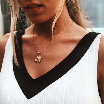 Colar dourado pendente redondo em mulher com vestido branco e preto