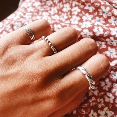 Mão com três anéis prateados sobre tecido floral bordô.