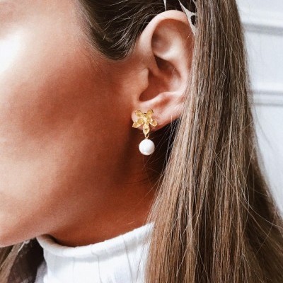 Brinco dourado com pérola pendente em orelha de mulher com cabelo castanho e camisola branca