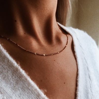 Colar dourado delicado no pescoço com camisa branca de malha.