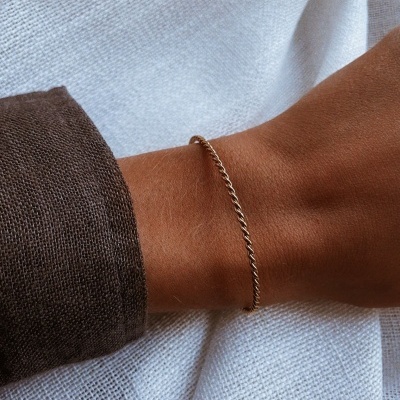 Pulso com pulseira fina dourada e mangas de camisa castanha sobre tecido branco