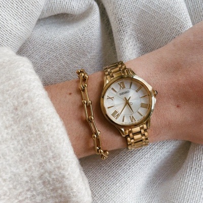 Relógio de pulso Seiko dourado com pulseira dourada e pulseira de elos no pulso