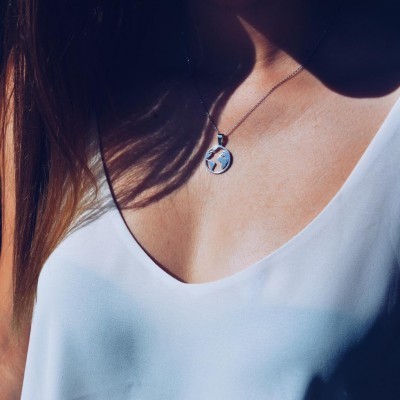 Colar prateado com pendente do mapa-múndi numa pessoa com blusa branca