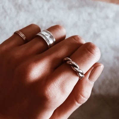 Mão com três anéis prateados diferentes e fundo desfocado