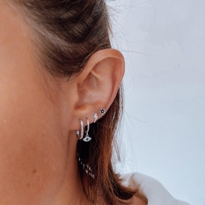 Orelha feminina com quatro brincos prateados distintos em fundo claro