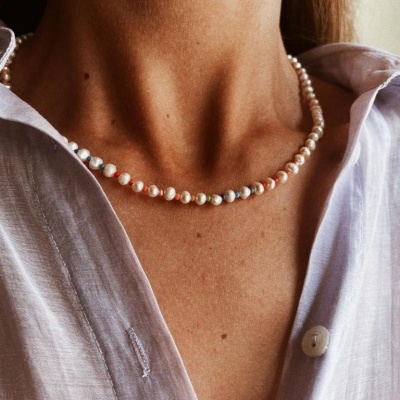 Colar de pérolas pequenas com contas coloridas intercaladas no pescoço de uma pessoa com camisa branca