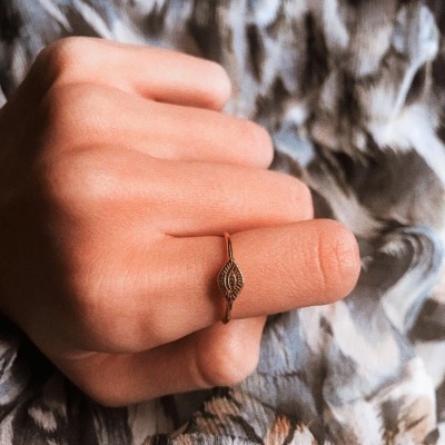 Anel dourado com detalhe decorativo no dedo indicador sobre tecido cinza e branco