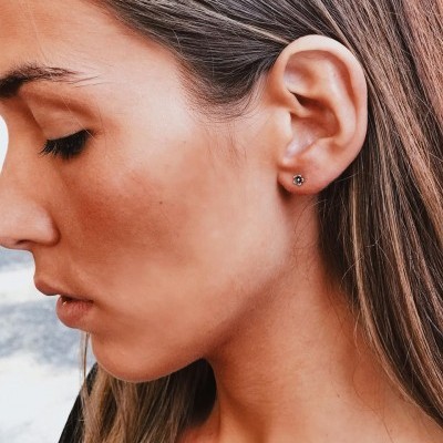 Brincos pequenos de prata com pedra escura no centro em orelha de mulher