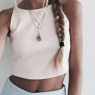 Mulher com top branco cropped, colares prateados e cabelo loiro trançado