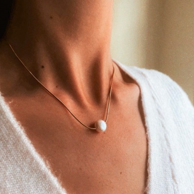 Colar dourado com pingente branco no pescoço, pessoa com casaco branco.