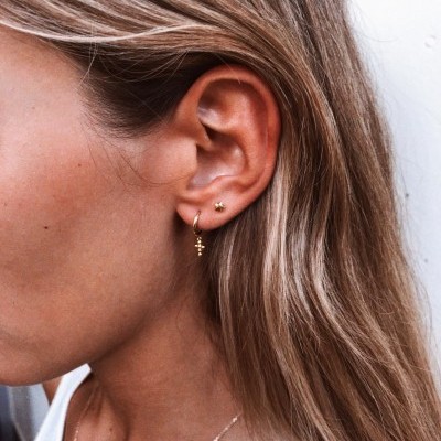 Brincos dourados cruz e estrela em orelha feminina com cabelo loiro