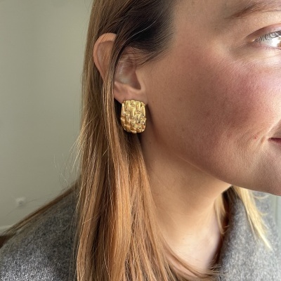 Brincos dourados quadrados com textura, usados por mulher