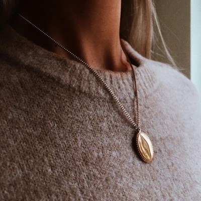 Colar dourado com pendente oval usado sobre blusa bege