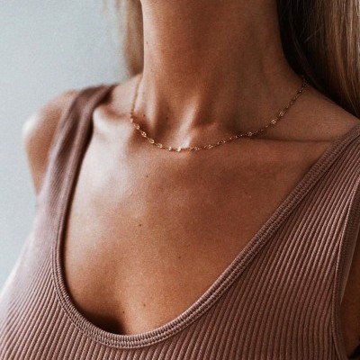 Colar delicado de corrente dourada usado com camisola castanha clara de malha canelada.