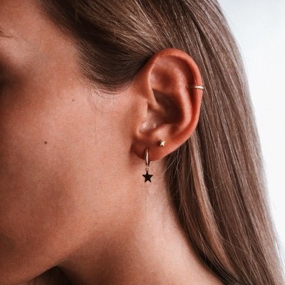 Orelha feminina com três brincos dourados, cabelo loiro ao fundo claro