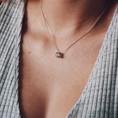 Colar prateado com pendente redondo sobre pele humana e top cinza canelado