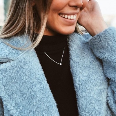 Mulher com casaco azul peludo e camisola preta com gargantilha prateada