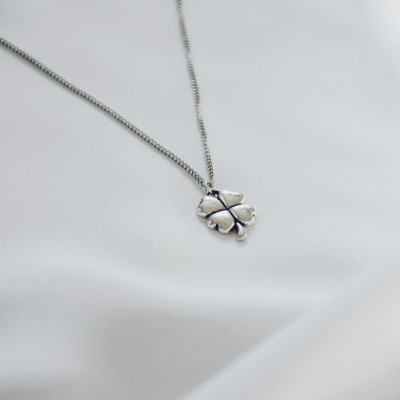 Colar com pendente em forma de folha de trevo prateado sobre tecido branco