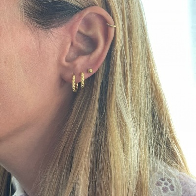 Orelha com quatro brincos dourados pequenos e cabelo loiro