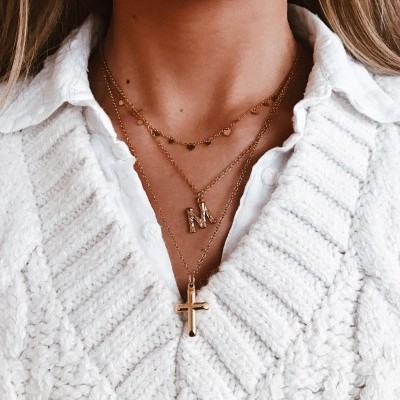 Colares dourados com letras e cruz sobre suéter branco de malha