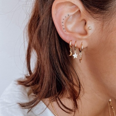 Orelha com brincos dourados pequenos com pendentes de lua, estrela e raio
