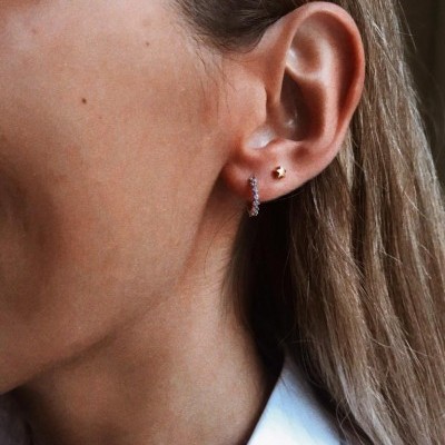 Orelha feminina com brincos prateados, cabelo castanho liso e camiseta branca