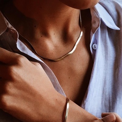 Pessoa a usar colar e pulseira dourados com camisa azul clara