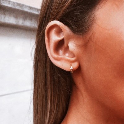 Brinco pequeno dourado com pedra branca numa orelha