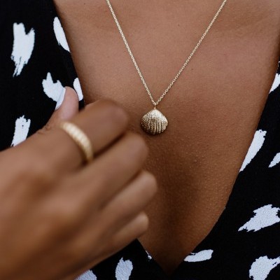 Colar dourado com pendente de concha e anel dourado em pele castanha com vestido preto e branco