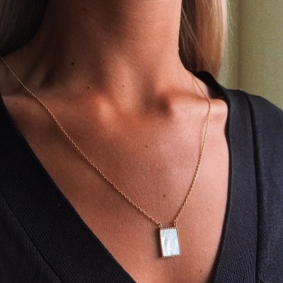 Colar dourado com pendente retangular branco numa mulher com roupa preta