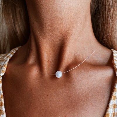 Colar com pendente redondo branco em cordão transparente no pescoço de pessoa com top xadrez amarelo e branco