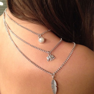 Colar triplo prateado com pingentes de pérola, 'LOVE' e pena num pescoço feminino