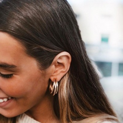 Brincos de argola dourados em orelha feminina com cabelo castanho e loiro.