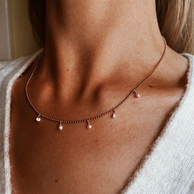 Colar dourado com pérolas numa pessoa com suéter branco