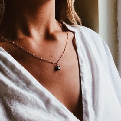 Colar delicado com pingente redondo preto e branco em mulher com camisa branca.