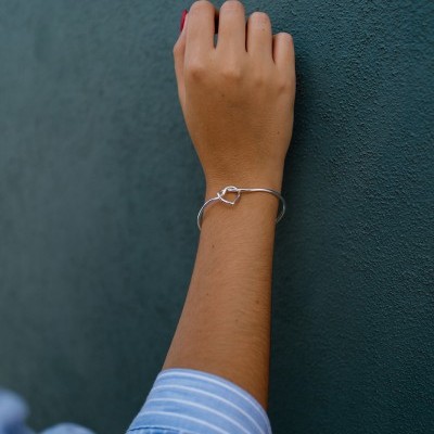 Braço com pulseira de metal prateado e nó decorativo junto a parede verde escura