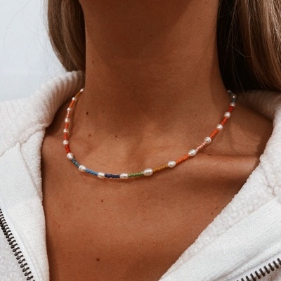 Colar colorido curto com contas pequenas e peroladas numa mulher com casaco branco