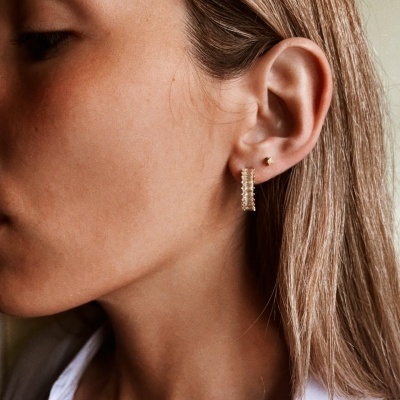 Brincos de argola dourados com textura esférica na orelha esquerda de mulher loira