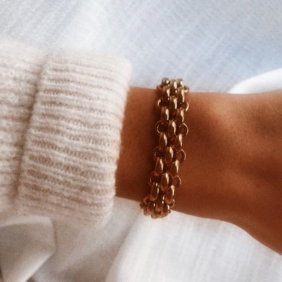 Pulseira dourada entrelaçada num pulso com camisola creme