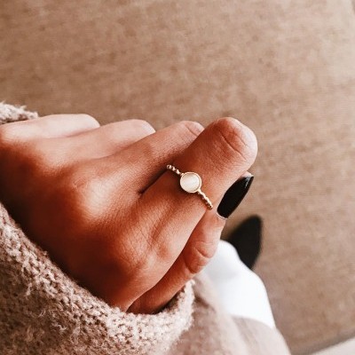 Anel dourado com pedra redonda branca e textura de bola na mão com manga bege