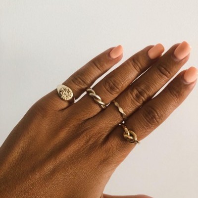 Mão com quatro anéis dourados de design variado sobre fundo branco