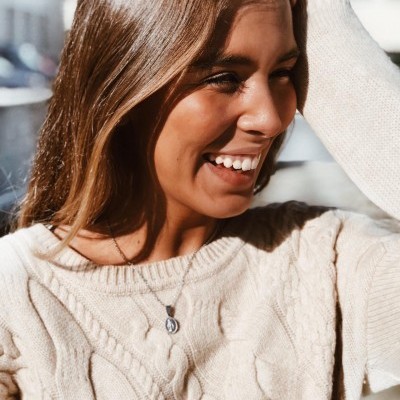 Mulher sorridente com suéter bege de malha grossa e colar prateado ao ar livre