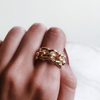 Anel dourado de corrente no dedo médio de mão com fundo branco