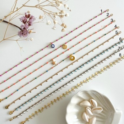 Oito pulseiras finas coloridas com pendentes sobre superfície branca com flores secas e conchas