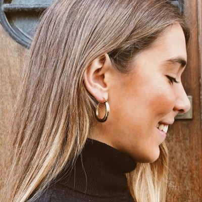 Brincos de argola dourados com textura retorcida usados por mulher e porta de madeira